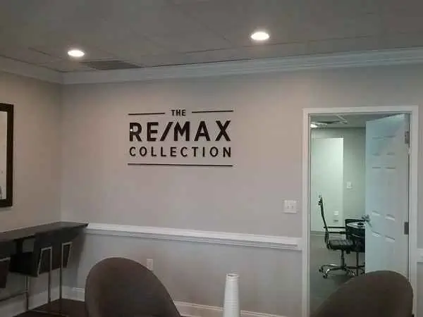 Interior of an office with a modern design, featuring a "RE/MAX Collection" sign on the wall and visible doorways to other rooms.