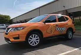 Orange Nissan SUV with "boost" branding showcasing car wraps parked in Greensboro.