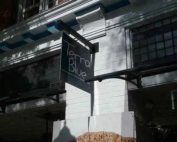 Exterior Blade Sign for Terra Blue coffee shop on a white brick wall, featuring blue accents and surrounded by shadows.